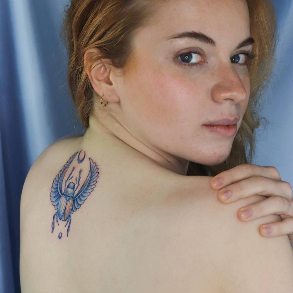 Kintsugi scarab tattoo located on the upper back, illustrative style.