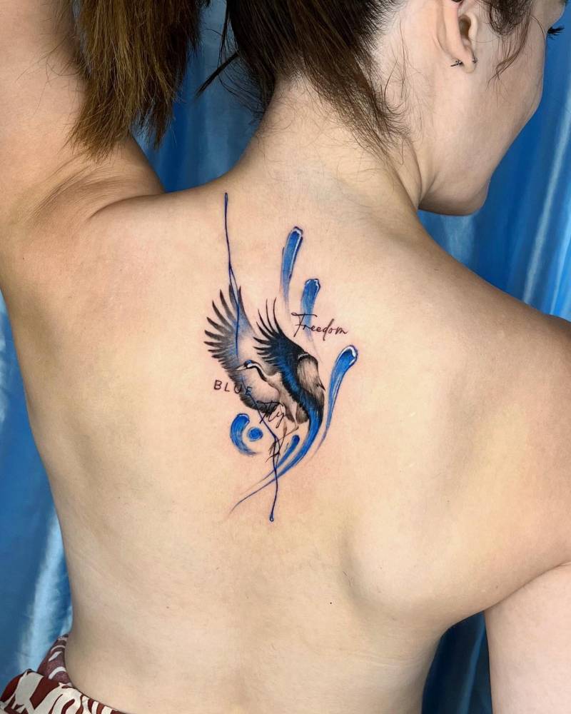 Blue crane and brush strokes tattoo located on the upper back.