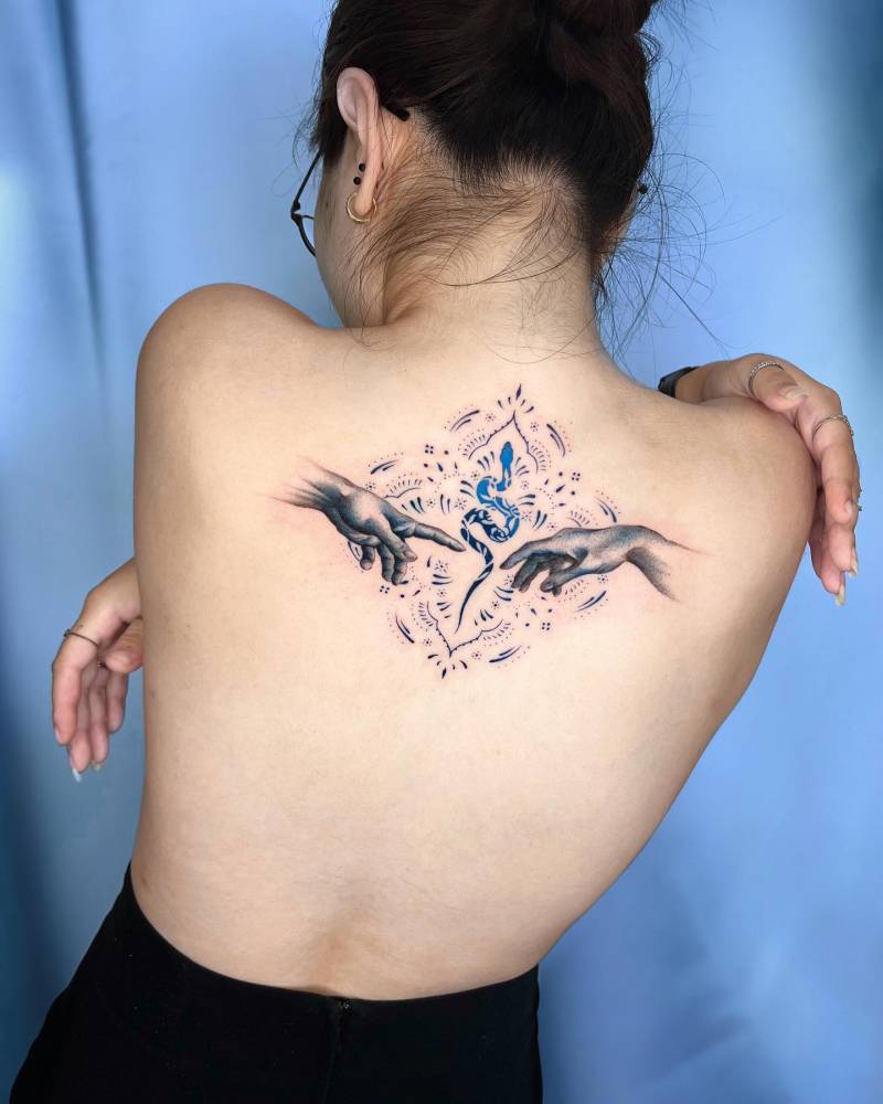The hands of creation tattooed on the upper back.