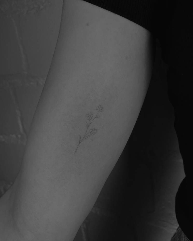 Fine line style forget-me-not flowers tattooed on the inner arm.