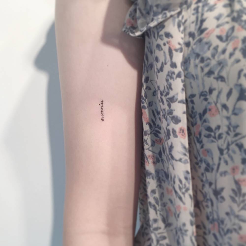 Tattoo of the word "eunoia" handwritten on the bicep.