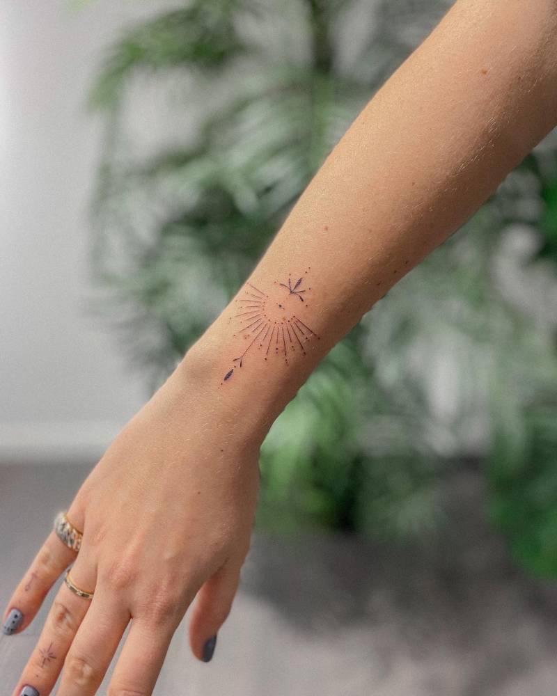 Fine line ornamental sun tattooed on the wrist.