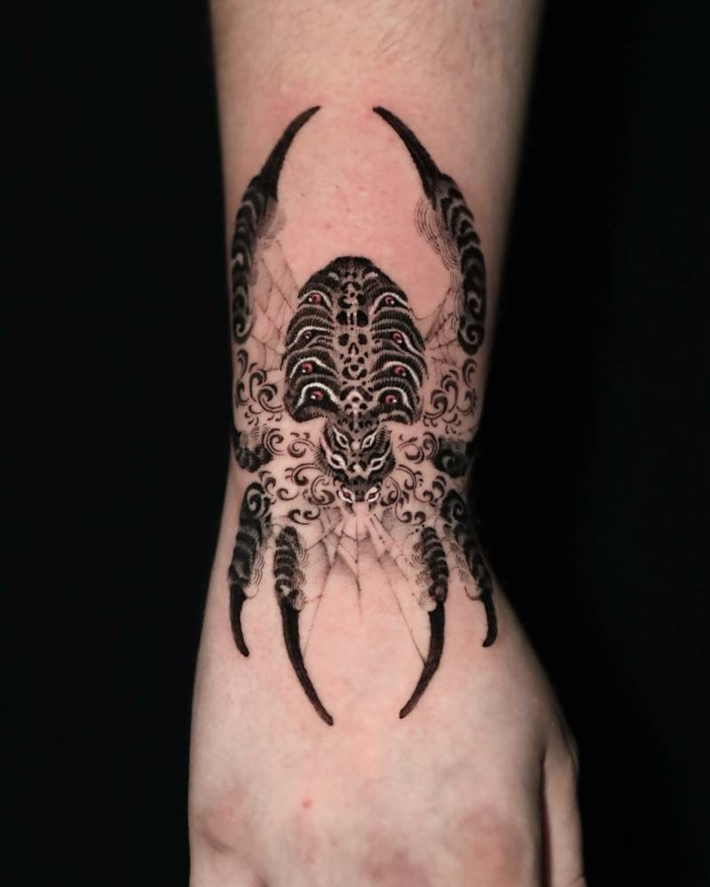 Spider tattoo located on the wrist, done in oriental style.