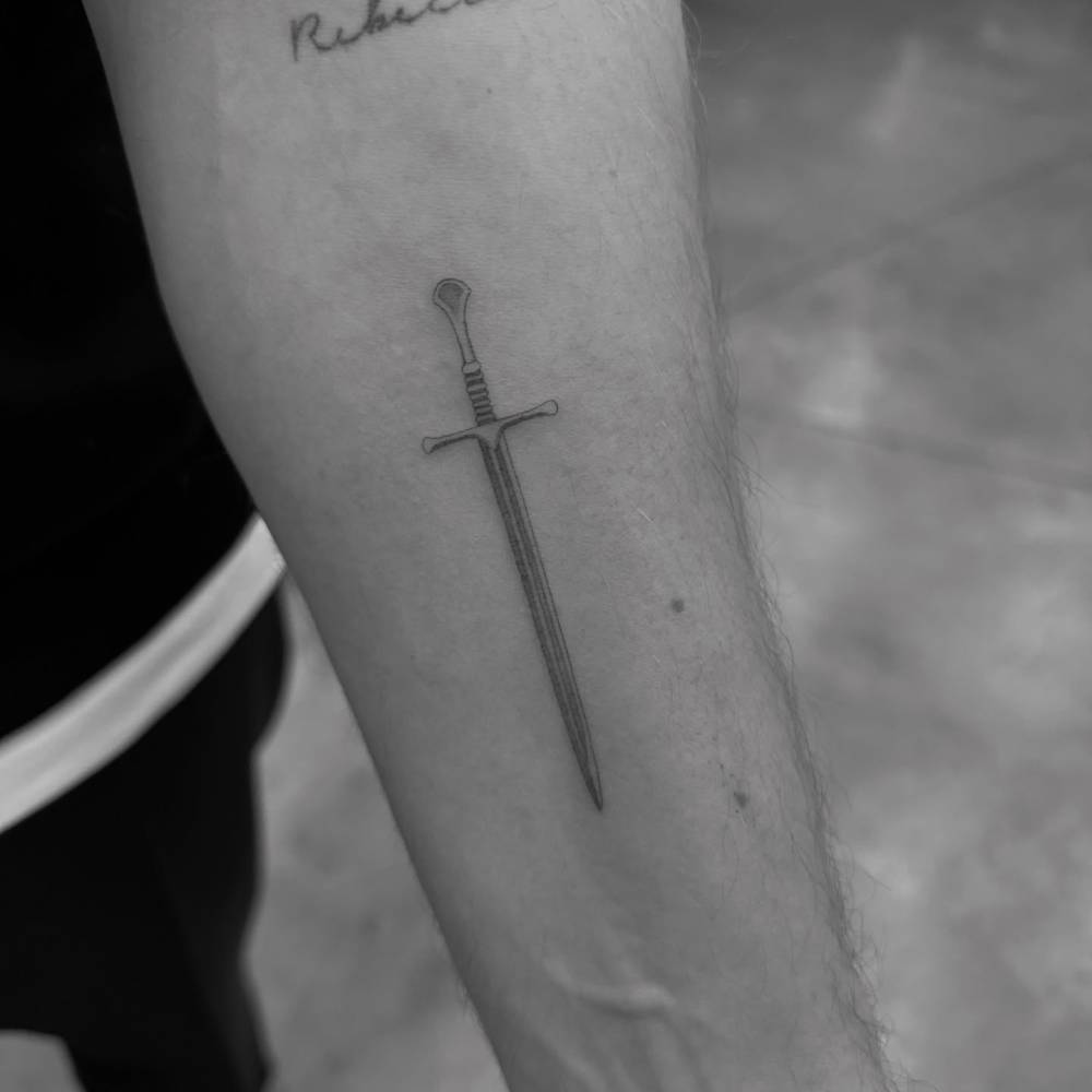 Little sword tattoo placed on the inner forearm, illustrative style.