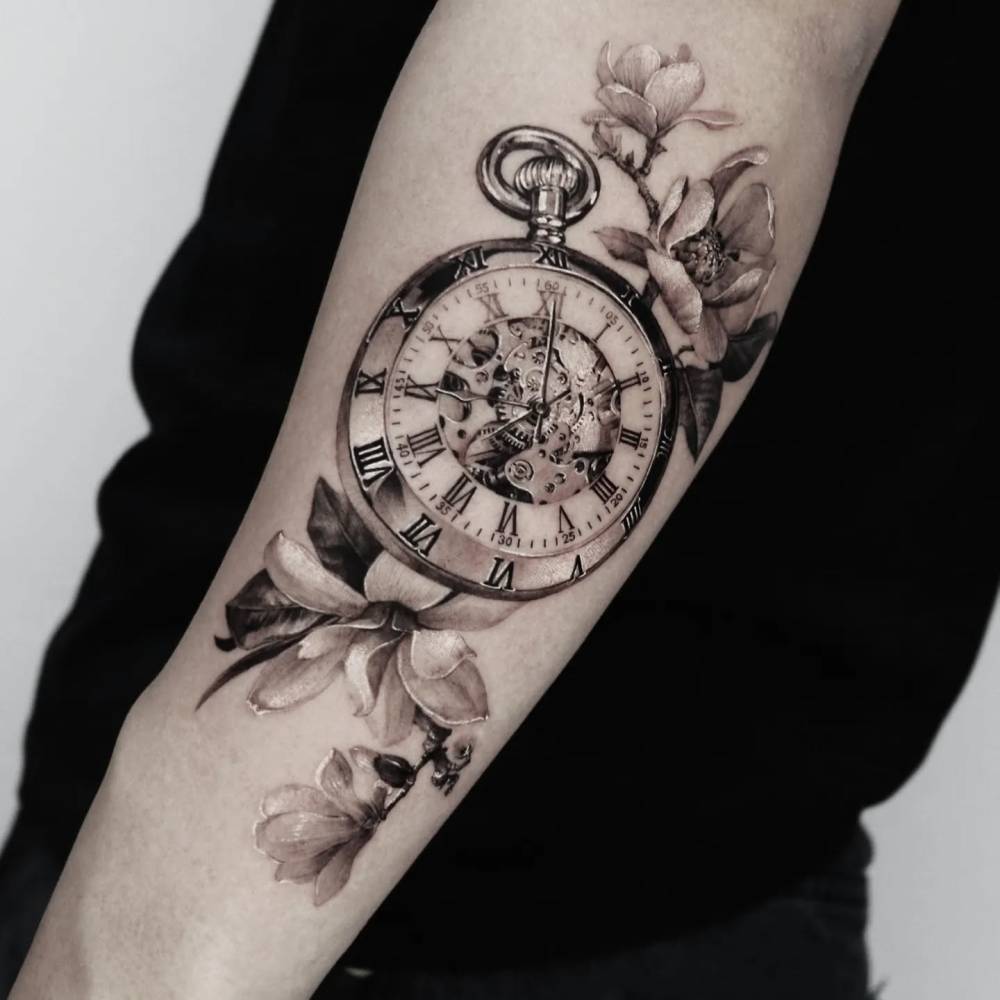 Pocket watch and magnolias tattoo located on the forearm.
