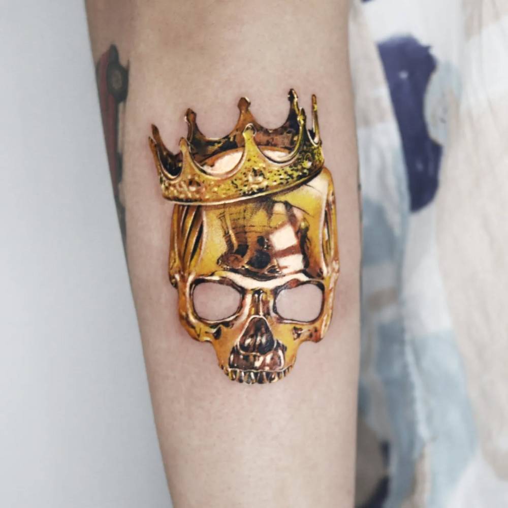 Golden crown and skull tattoo located on the forearm.