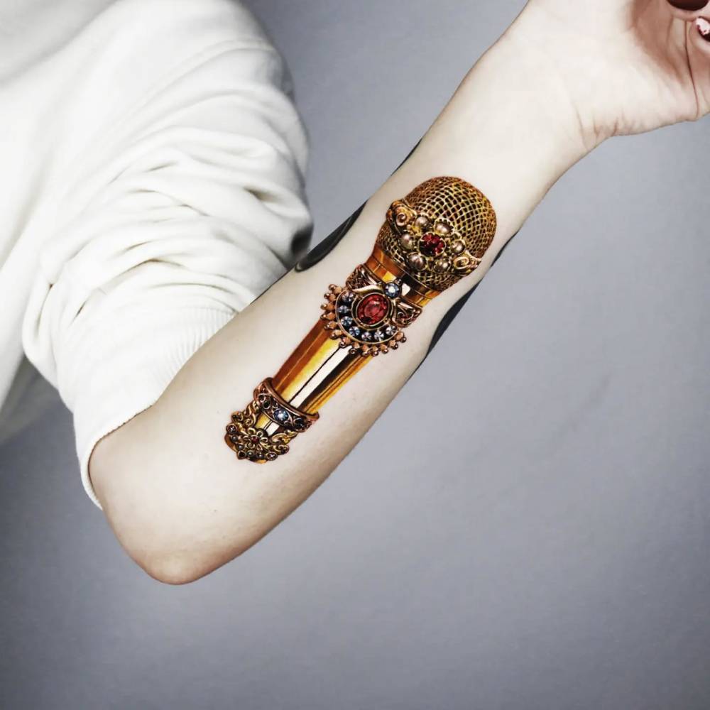 Gold microphone tattoo in micro-realistic style located on the inner forearm.