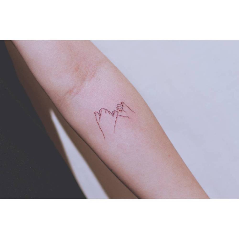 Fine line style pinky promise tattoo located on the inner forearm.