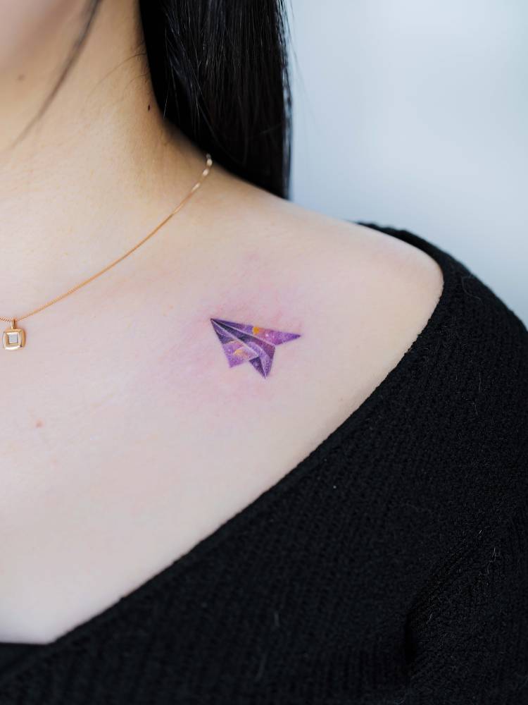 Watercolor style paper plane tattoo done on the collarbone.