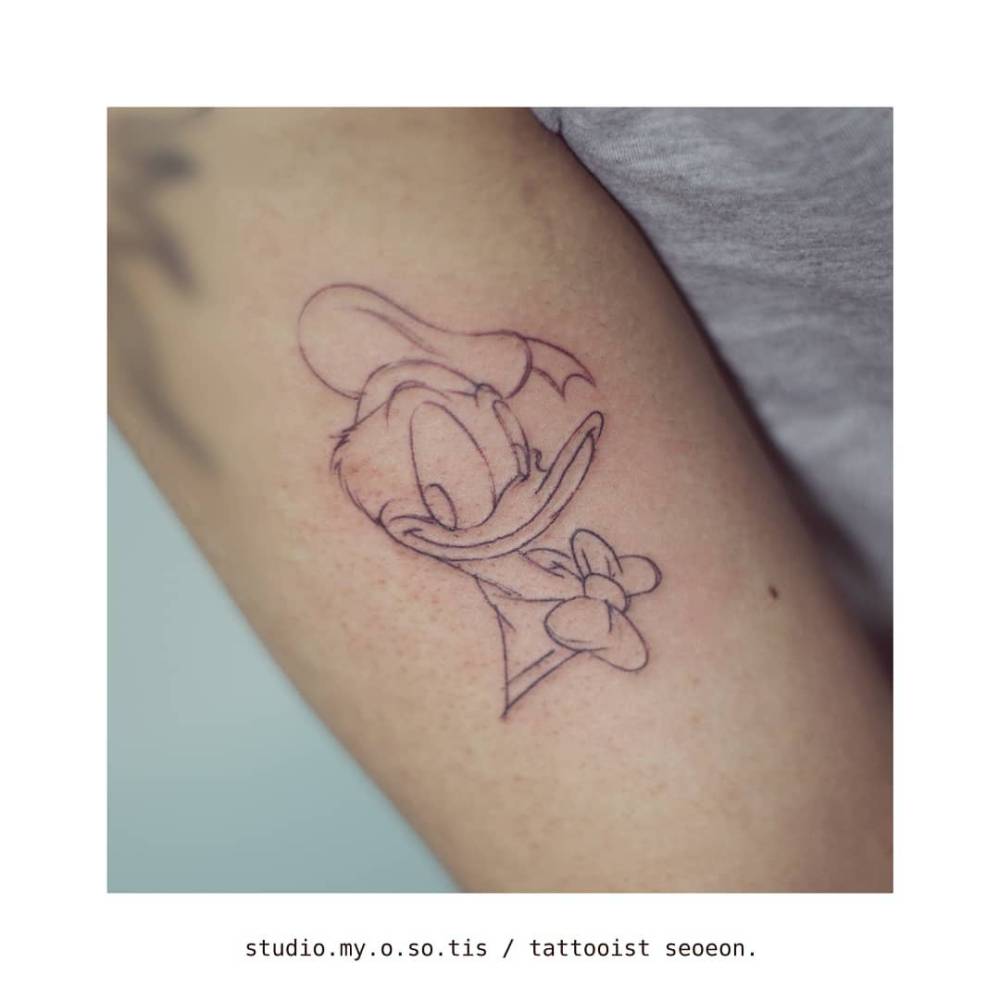 Donald Duck portrait tattoo in cartoon style located on the upper arm.