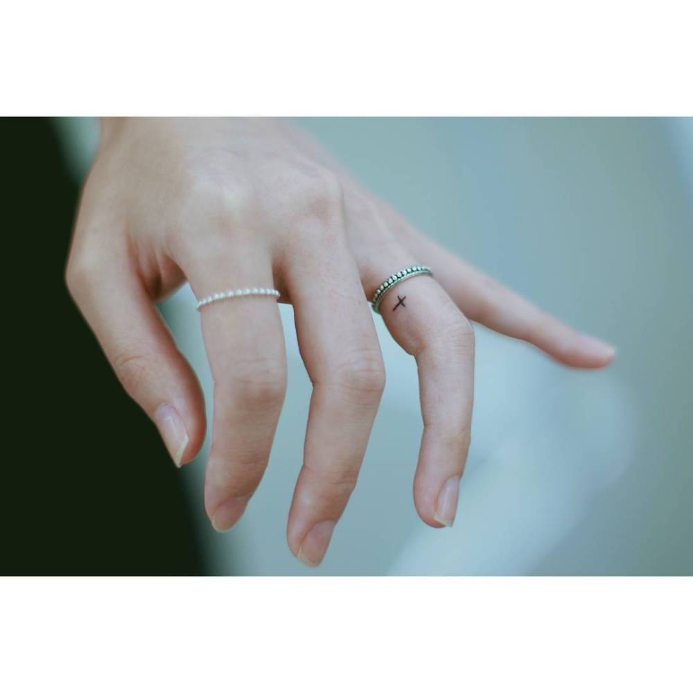 Tiny minimalistic cross tattoo located on the finger.