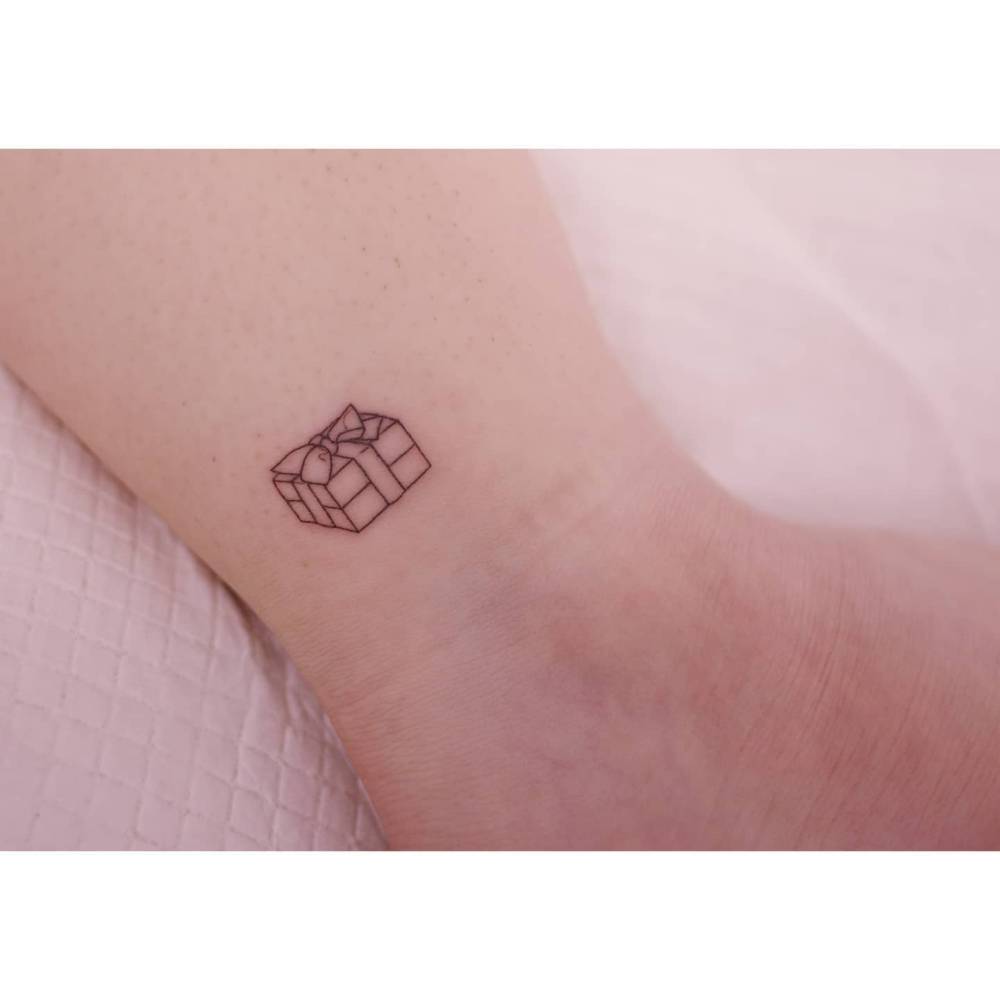 Little present box tattoo in fine line located on the ankle.