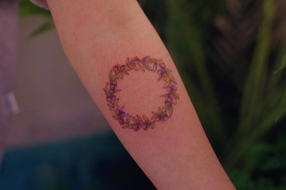 Flower wreath tattoo in illustrative style placed on the inner forearm.