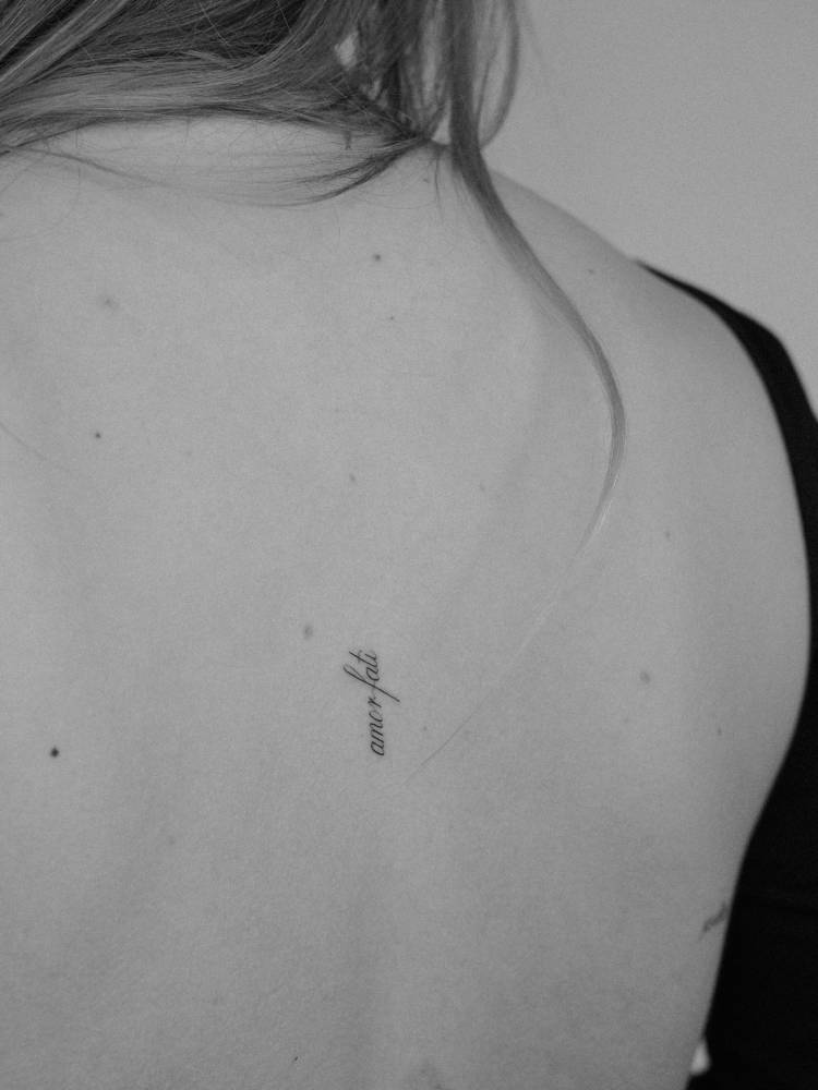"Amor fati" lettering tattoo placed on the back.