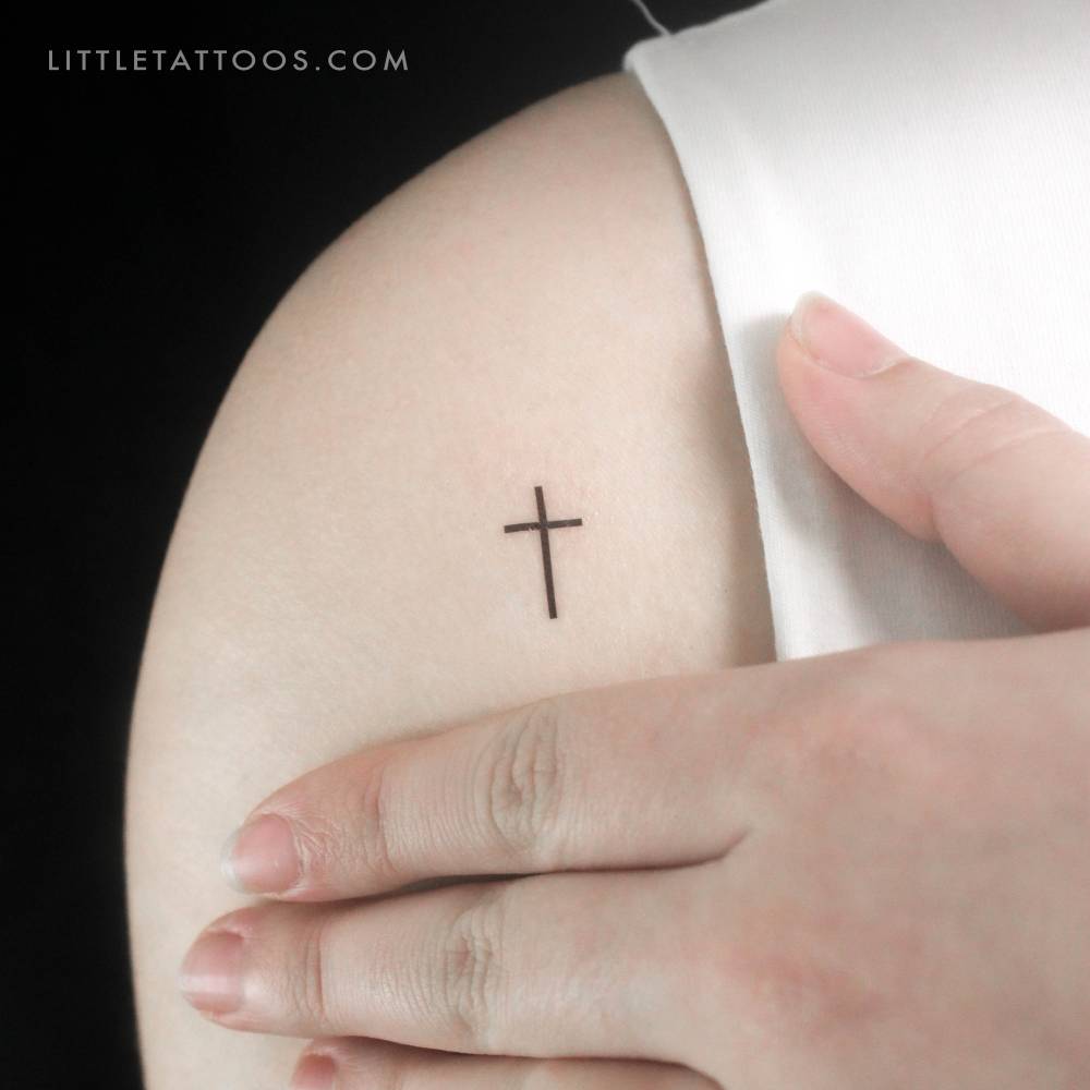 Minimalist style tiny cross temporary tattoo located on the shoulder.