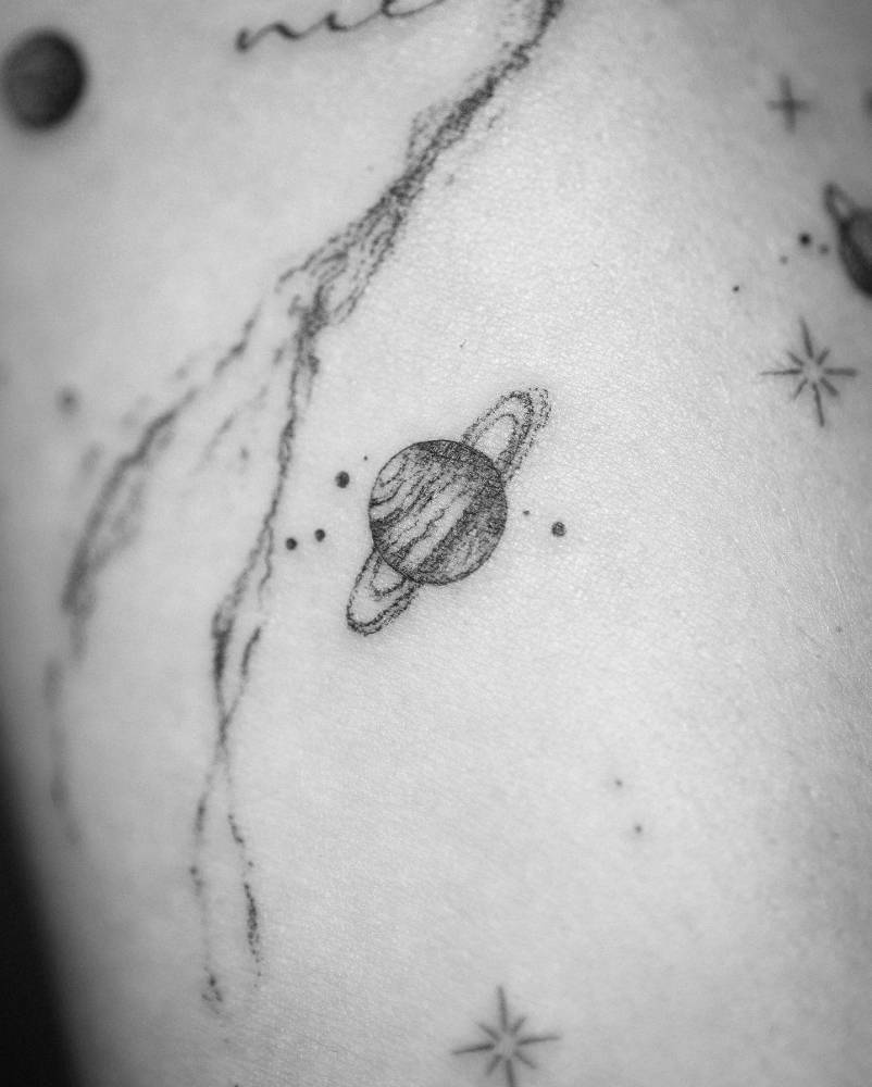 Little Saturn tattoo in illustrative style located on the inner forearm.