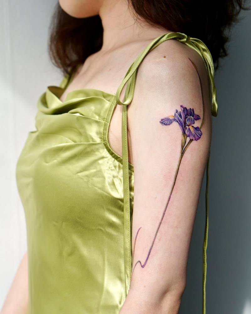 Watercolor style iris flower tattoo located on the upper arm.