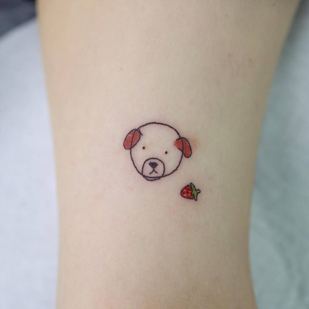 Cartoon style dog portrait and strawberry tattoo located on the bicep.