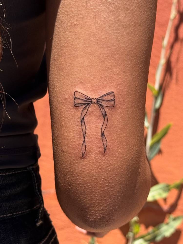 Bow tattoo in illustrative style located on the tricep.