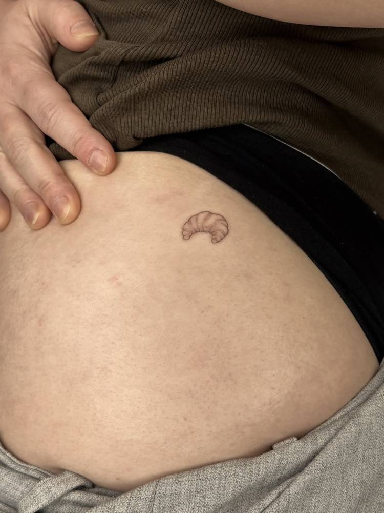 Tiny fine line style croissant tattoo located on the hip.