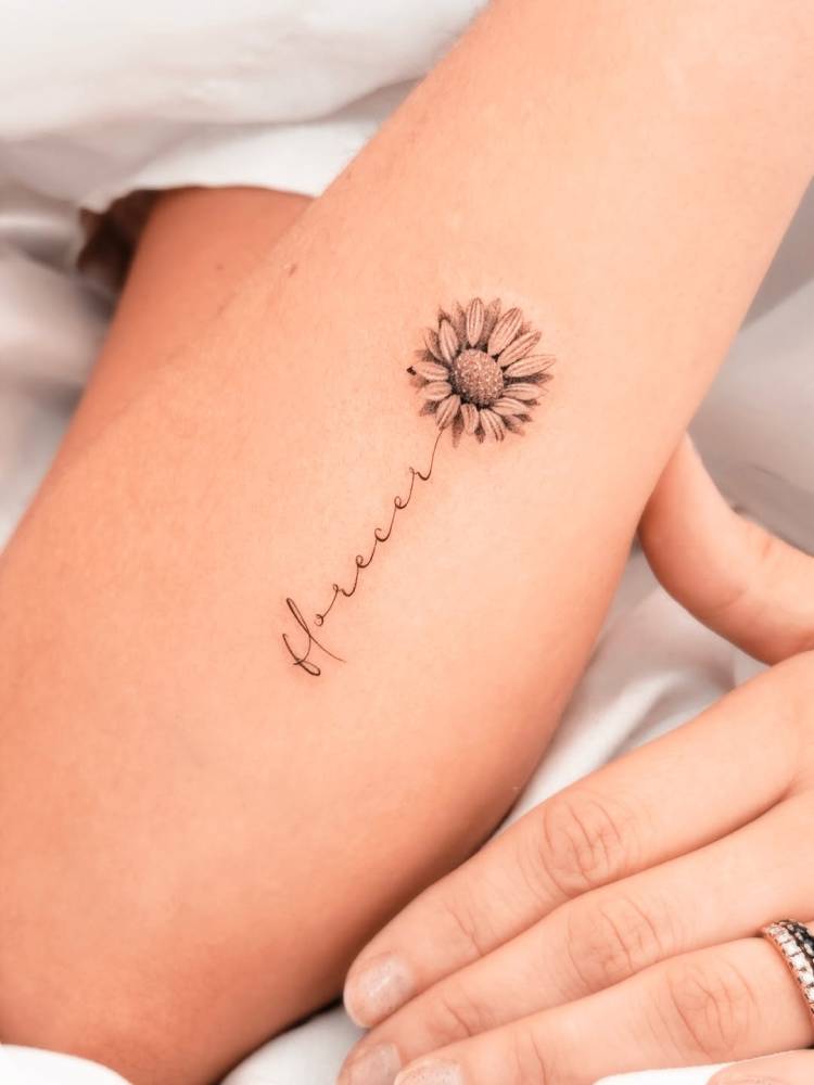 Micro-realistic style sunflower and word "florecer" tattoo located on the forearm.