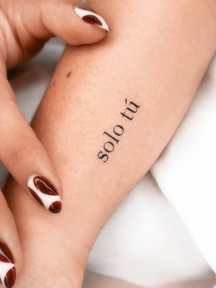 "Solo tú" lettering tattoo located on the wrist.