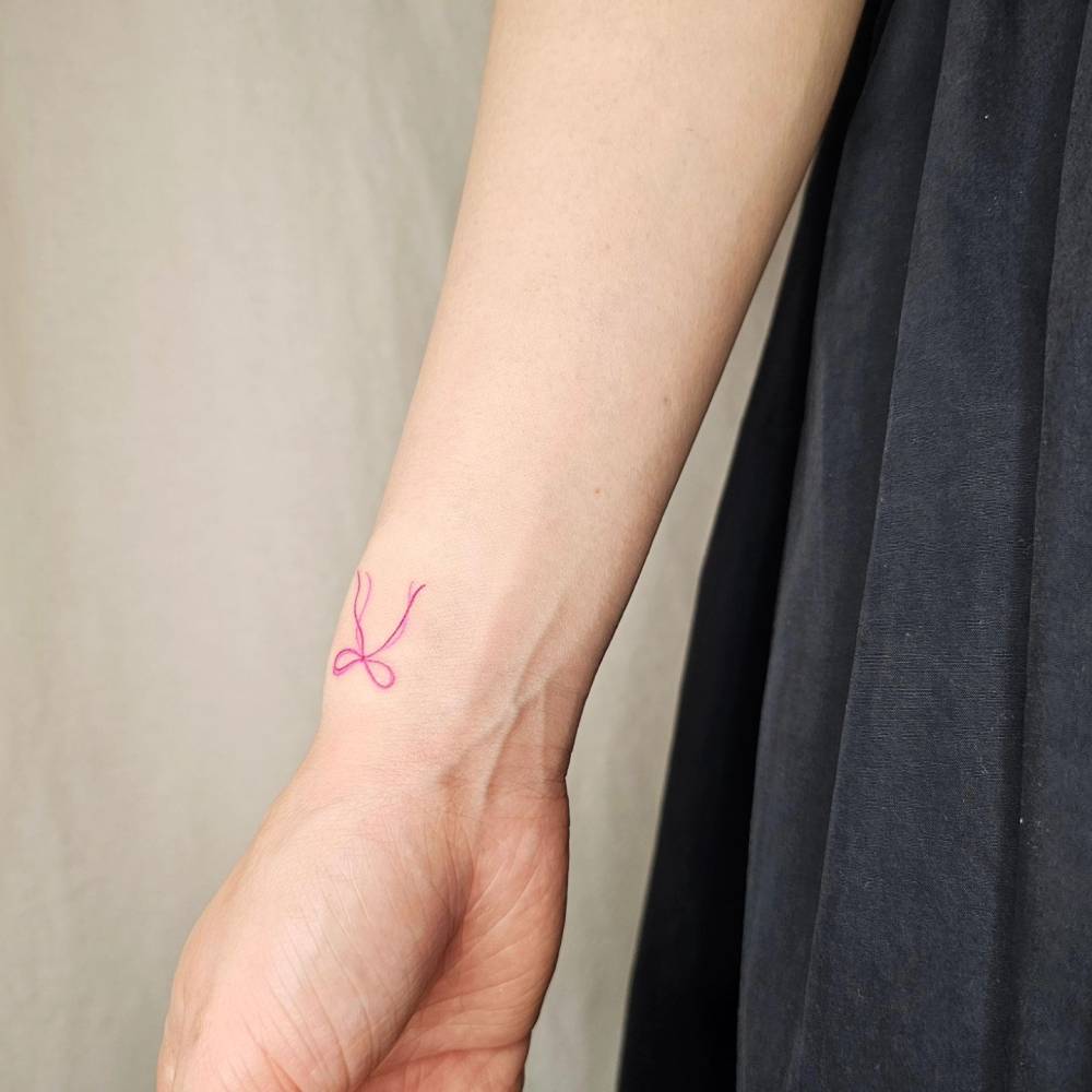 Watercolor style bow tattoo located on the wrist.