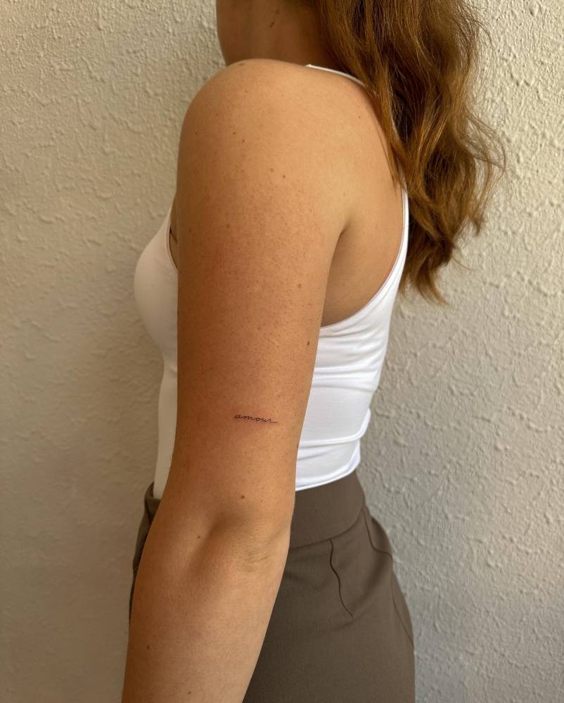Tattoon of the word "amour" handwritten on the tricep.