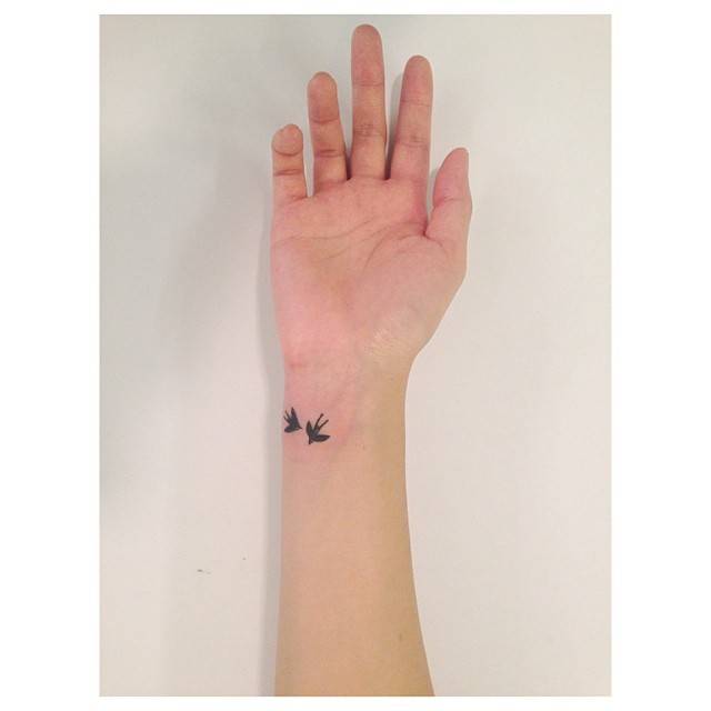 Flying swallows tattoo located on the wrist, done in minimalistic style.