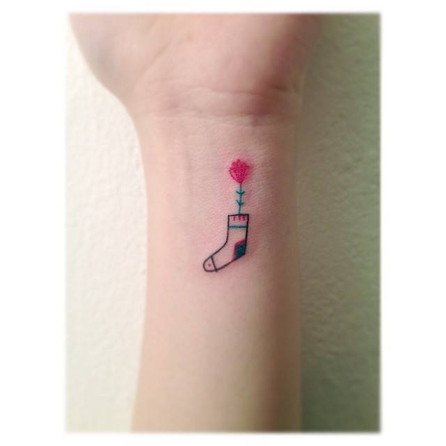Sock and flower tattoo in minimalistic style located on the wrist.