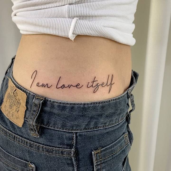 "I am love itself" lettering tattoo placed on the hip.