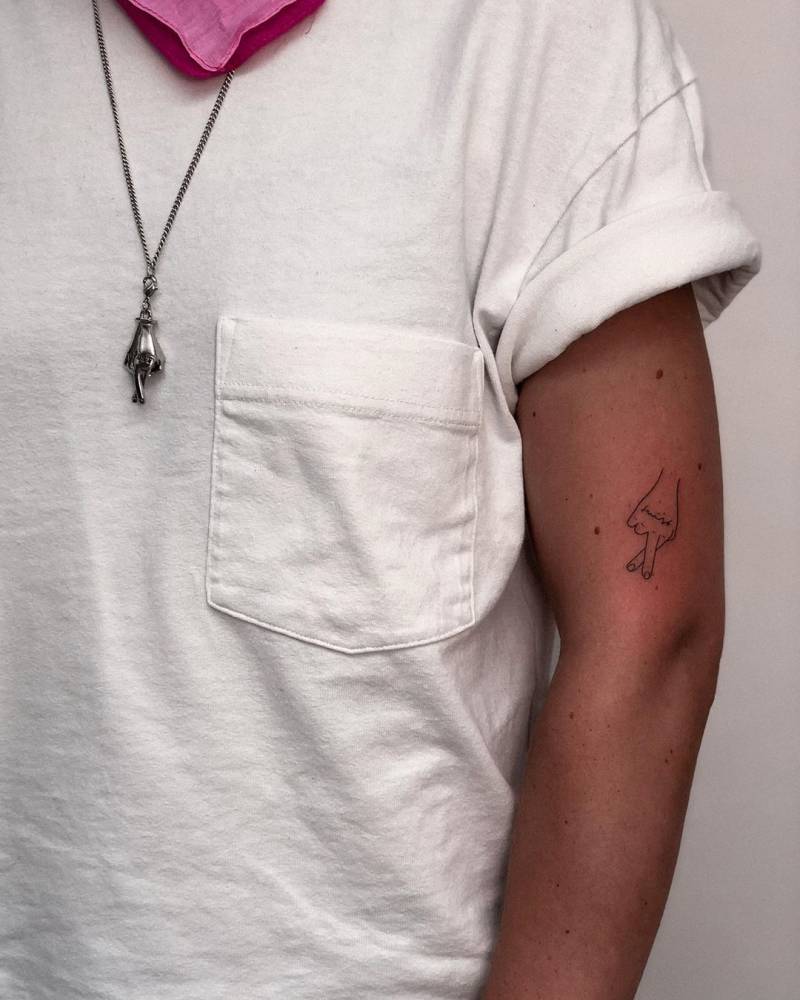 Minimalistic style crossed fingers tattoo hand poked on the upper arm.