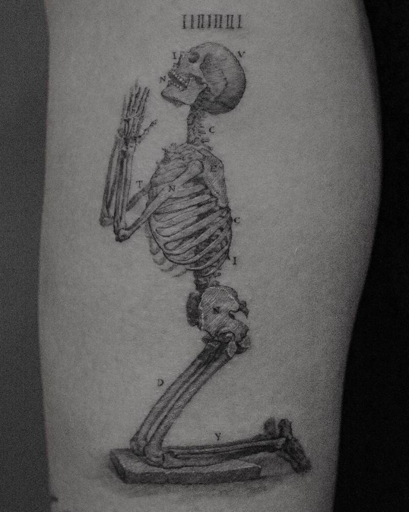 Micro-realistic style praying skeleton tattoo located on the tricep.