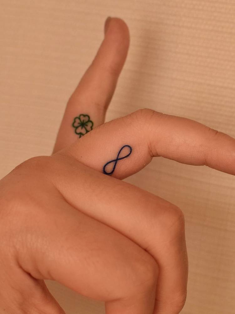 Four leaf clover and infinity symbol tattooed on the fingers.