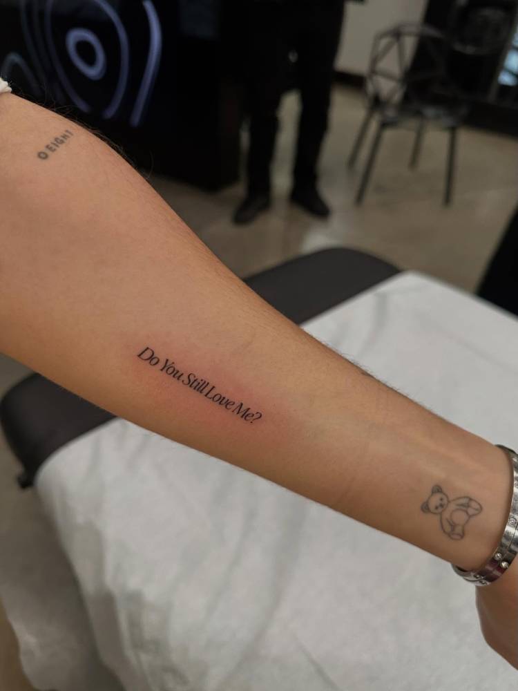 "Do you still love me?" lettering tattoo located on the inner forearm.