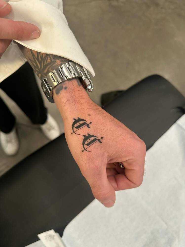 Two initials "C" in gothic font tattooed on the hand.