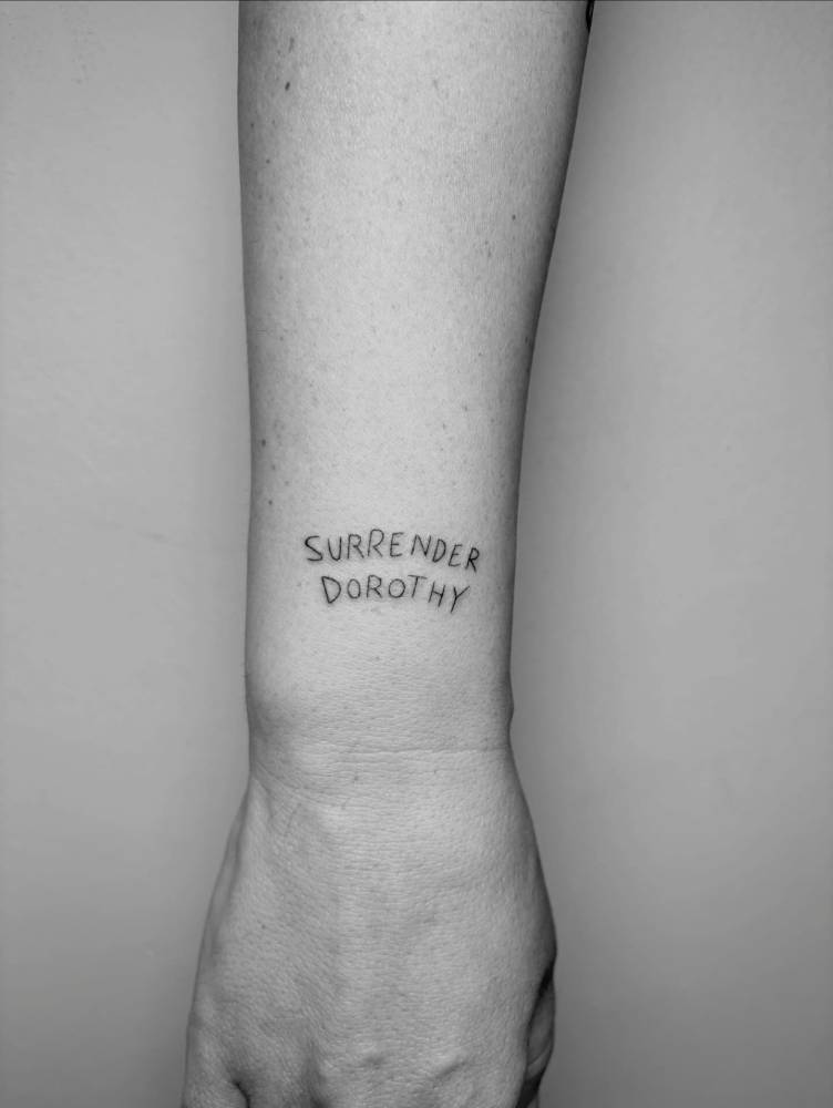 "Surrender Dorothy" lettering tattoo located on the wrist.