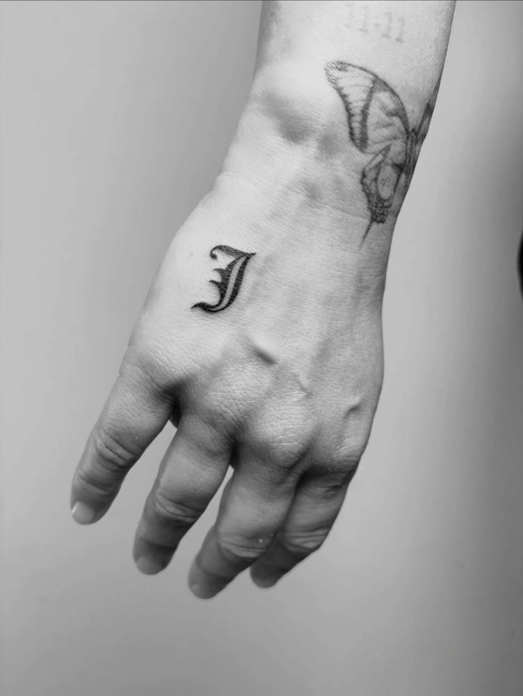 Letter "J" tattoo in gothic font located on the hand.