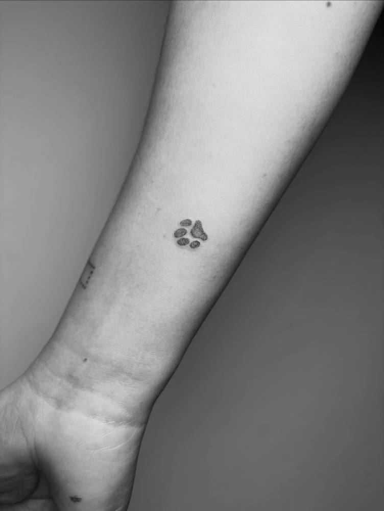 Little dog paw print tattoo in dotwork style located on the wrist.
