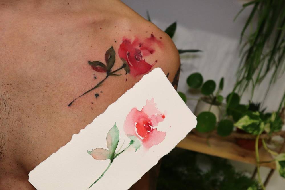 Red rose tattoo in watercolor style located on the shoulder.