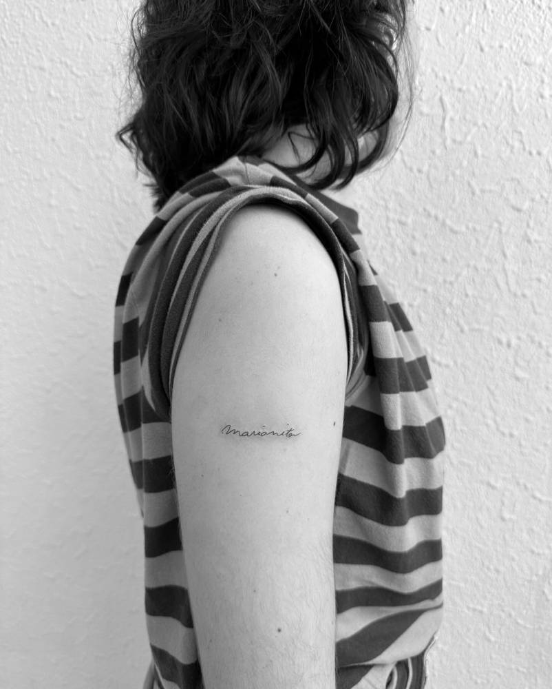 "Marianita" lettering tattoo handwritten on the upper arm.