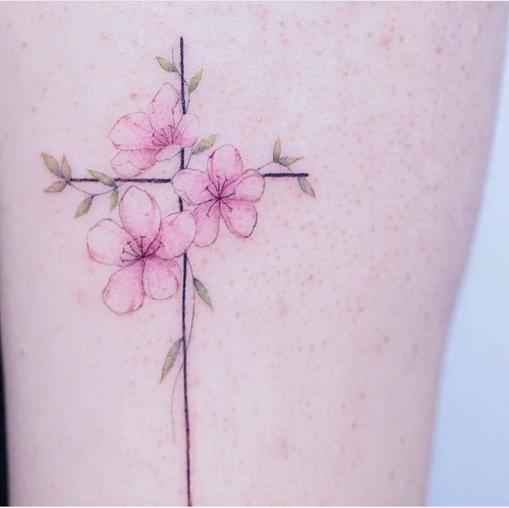 Watercolor flower cross tattoo on the upper arm.