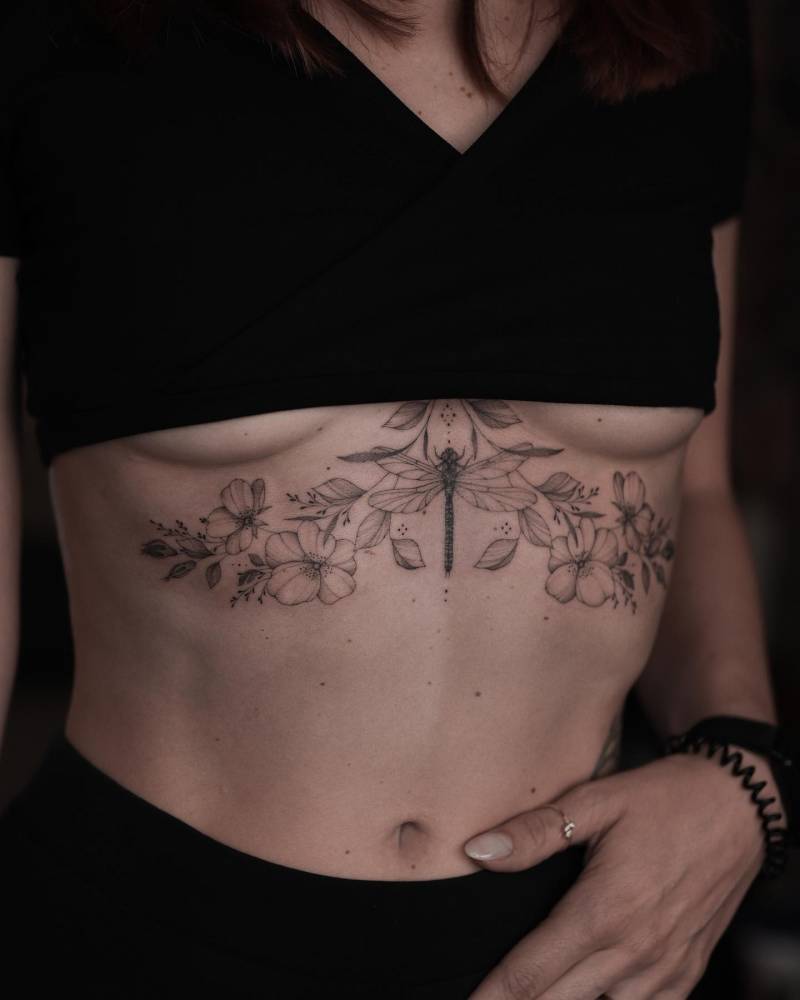 Dog roses and dragonfly tattoo located on the stomach.