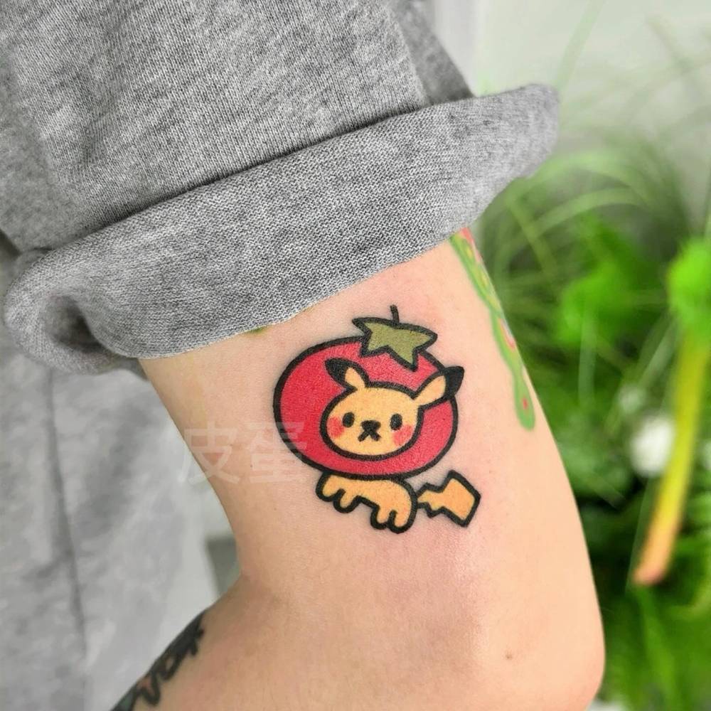 Pikachu and tomato tattoo located on the upper arm, done in cartoon style.