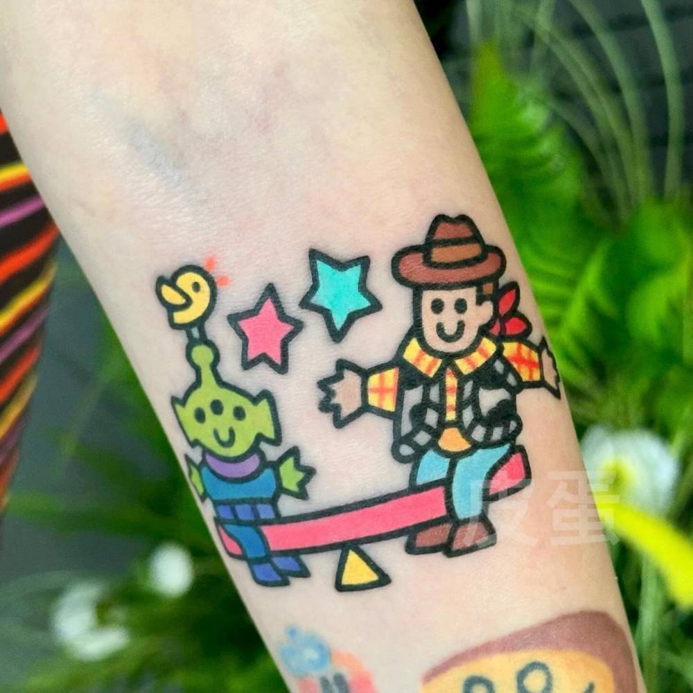 Toy Story Alien and Woody tattoo located on the inner forearm, cartoon style.