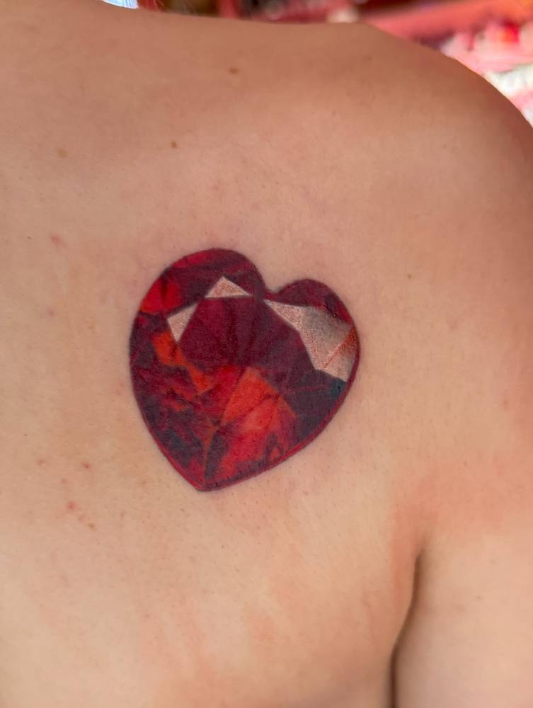 Ruby heart tattoo in realistic style placed on the shoulder blade.