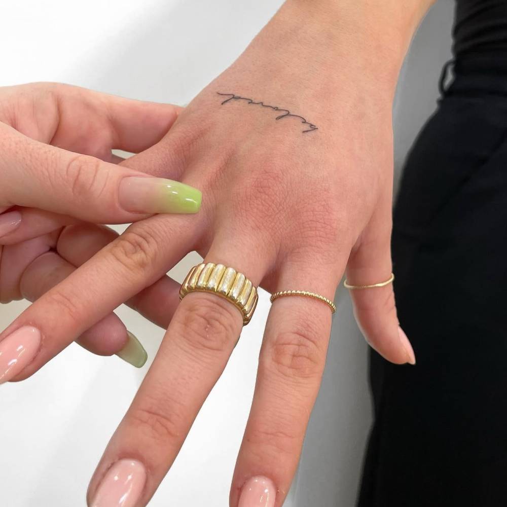 Handwritten font word "beloved" tattooed on the hand.