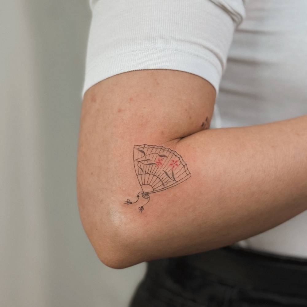 Hand fan tattoo in fine line style located on the elbow.