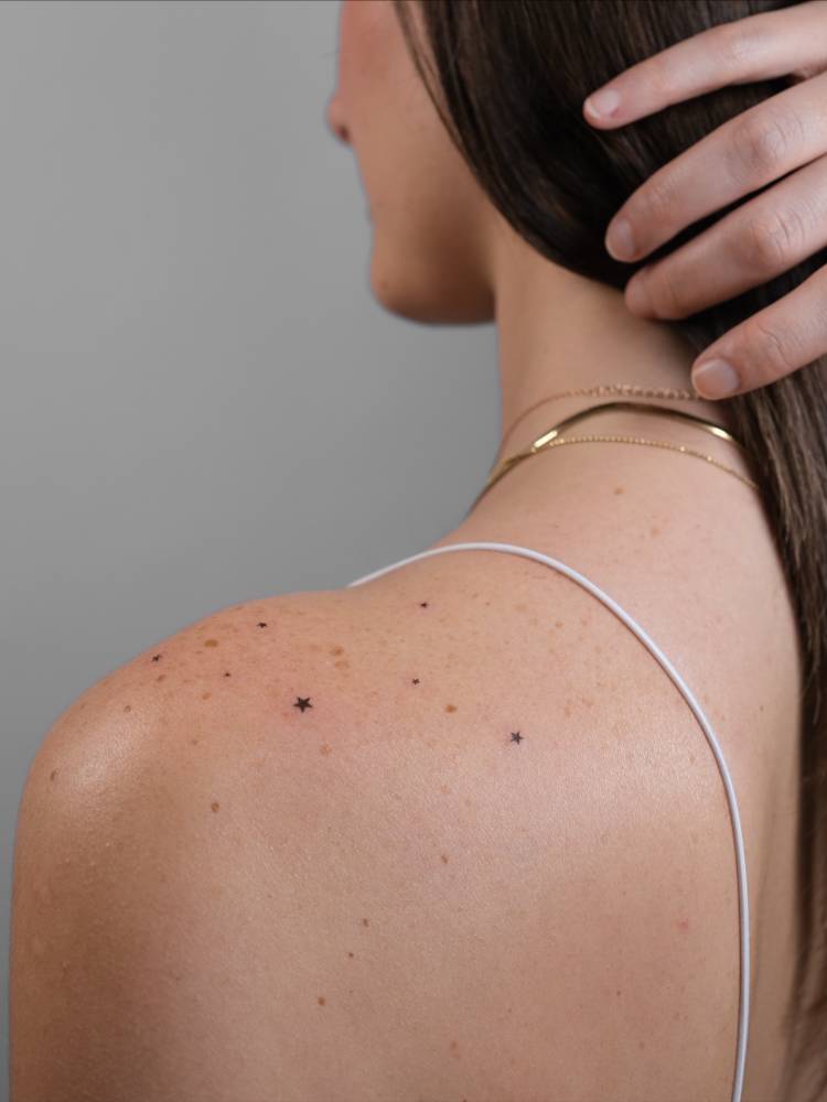 Minimalistic style star freckles tattoo located on the shoulder.