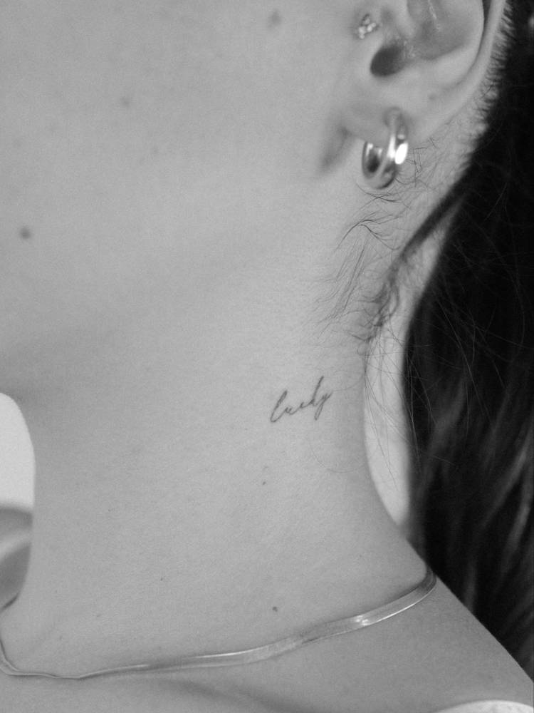 Word "lucky" in handwritten font tattooed on the neck.